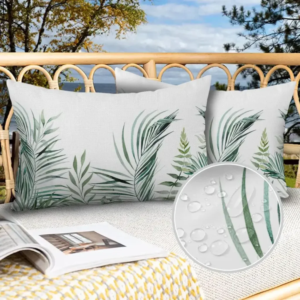 White tropical throw pillows with green leaf patterns on a wicker outdoor sofa.