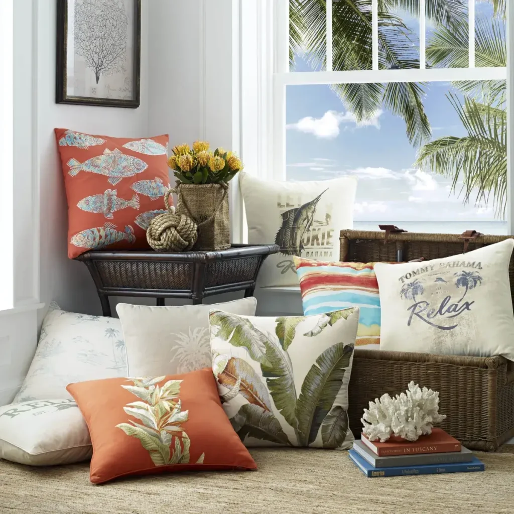 Assorted tropical and beach-inspired throw pillows arranged near a window with palm trees outside.